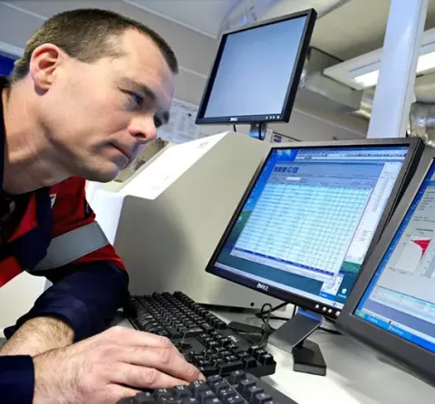 A technician analyzes a sample result showing on a lab computer screen